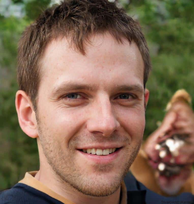 Smiling man outdoors with greenery background.